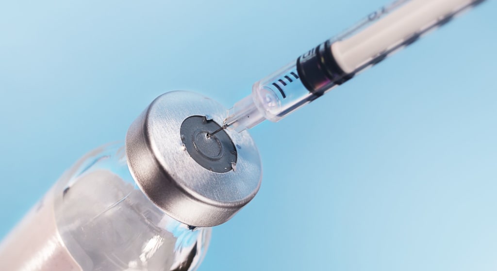 A syringe needle is inserted into the rubber stopper of a glass vial containing a clear liquid, possibly bpc 157 peptide, against a blue background.